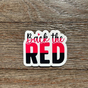 K&ouml;nnte beinhalten: Ein wei&szlig;er Aufkleber mit dem Text "Back the Red" in schwarzer und pinkfarbener Schrift. Das Wort "Red" ist in zwei H&auml;lften geteilt, wobei die obere H&auml;lfte pink und die untere H&auml;lfte schwarz ist.