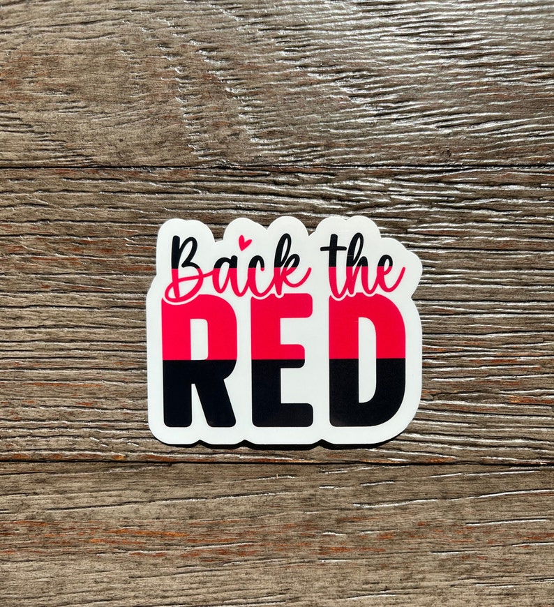 K&ouml;nnte beinhalten: Ein wei&szlig;er Aufkleber mit dem Text "Back the Red" in schwarzer und pinkfarbener Schrift. Das Wort "Red" ist in zwei H&auml;lften geteilt, wobei die obere H&auml;lfte pink und die untere H&auml;lfte schwarz ist.