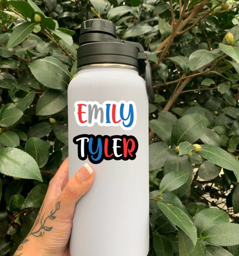 May include: White water bottle with a black lid and handle. The bottle has a sticker with the names "Emily Tyler" in red, blue, and black lettering.