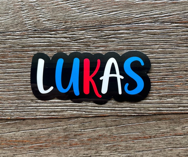 May include: A black sticker with the name "LUKAS" written in white, blue, and red letters.