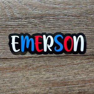 May include: Black vinyl sticker with the name "EMERSON" in white letters with blue and red accents.