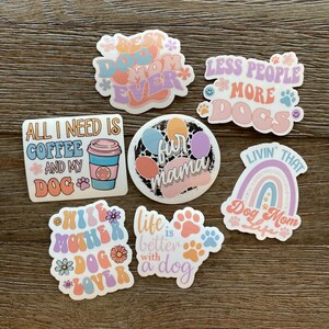 K&ouml;nnte beinhalten: Ein Set aus neun bunten Aufklebern mit Spr&uuml;chen zum Thema Hund. Die Aufkleber zeigen Pfotenabdr&uuml;cke, Regenb&ouml;gen, Kaffeetassen und Blumen. Der Text auf den Aufklebern lautet: "Best Dog Mom Ever", "All I Need Is Coffee And My Dog", "Fun Mama", "Less People More Dogs", "Wife Mother Dog Lover", "Life Is Better With A Dog", und "Livin' That Dog Mom Life".