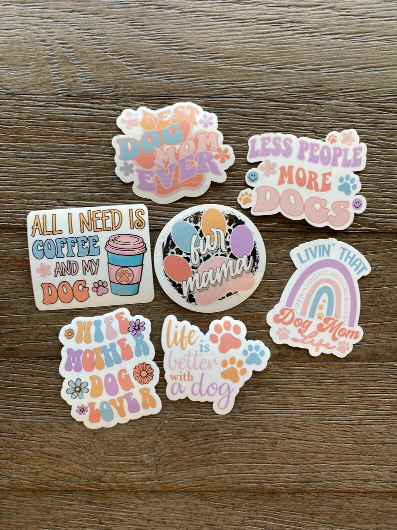 K&ouml;nnte beinhalten: Ein Set aus neun bunten Aufklebern mit Spr&uuml;chen zum Thema Hund. Die Aufkleber zeigen Pfotenabdr&uuml;cke, Regenb&ouml;gen, Kaffeetassen und Blumen. Der Text auf den Aufklebern lautet: "Best Dog Mom Ever", "All I Need Is Coffee And My Dog", "Fun Mama", "Less People More Dogs", "Wife Mother Dog Lover", "Life Is Better With A Dog", und "Livin' That Dog Mom Life".