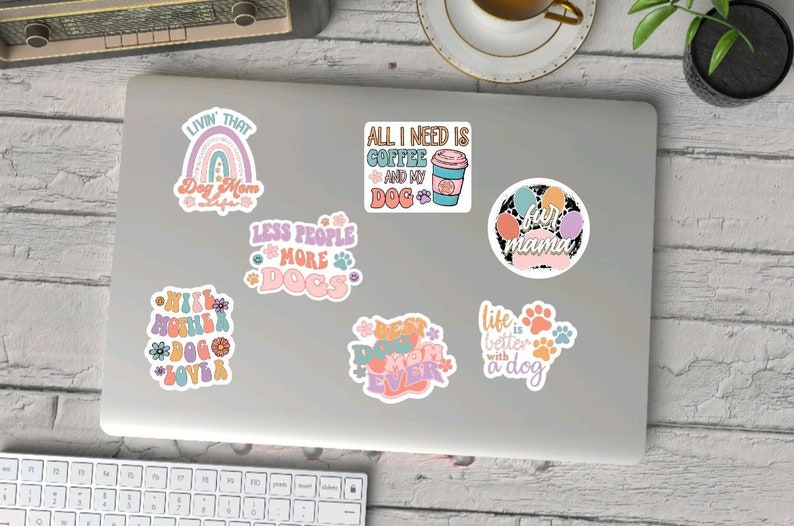 K&ouml;nnte beinhalten: Ein Set mit 8 Hundestickern mit bunten Pfotenabdr&uuml;cken, Regenb&ouml;gen und Text. Die Sticker enthalten S&auml;tze wie "Livin' That Dog Mom Life", "Less People More Dogs", "All I Need Is Coffee And My Dog", "Best Dog Mom Ever", "Life Is Better With A Dog" und "Fur Mama".