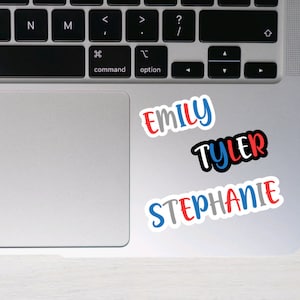 May include: Three colorful name stickers on a silver laptop. The names are "Emily", "Tyler", and "Stephanie".