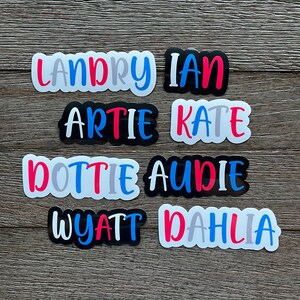 May include: Eight colorful name stickers with white backgrounds. The names are Landry, Ian, Artie, Kate, Dottie, Audie, Wyatt, and Dahlia.