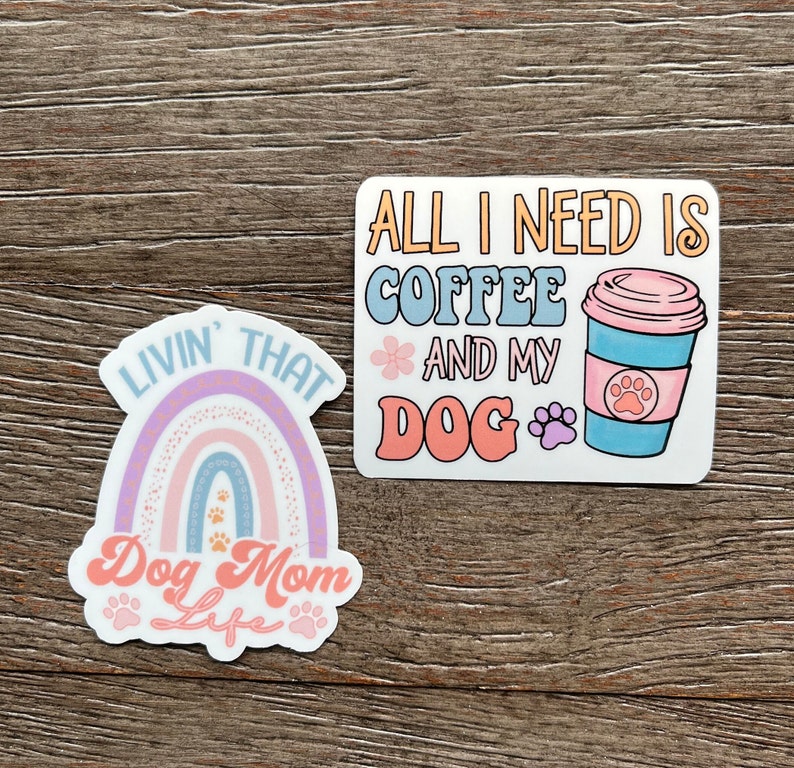 K&ouml;nnte beinhalten: Zwei Aufkleber mit Hunde-Motiven. Der erste Aufkleber zeigt einen Regenbogen mit Pfotenabdr&uuml;cken und den Text "Livin' That Dog Mom Life". Der zweite Aufkleber zeigt eine Kaffeetasse mit einem Pfotenabdruck und den Text "All I Need Is Coffee And My Dog".