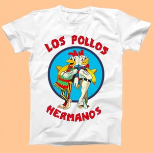 May include: White t-shirt featuring a graphic of two cartoon chickens wearing sombreros and the text "Los Pollos Hermanos".