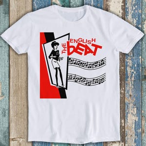 May include: White t-shirt with a red, black, and white graphic design. The graphic features a woman in a skirt and the text "The English Beat".