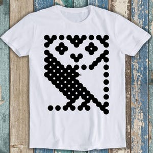 Może przedstawiać: Biały t-shirt z krótkim rękawem z dużym, wyśrodkowanym nadrukiem sowy. Sowa składa się z serii połączonych ze sobą czarnych kółek i kropek, tworząc stylizowaną, geometryczną sylwetkę na tle gładkiego, białego materiału koszulki.