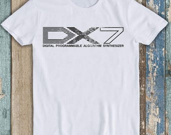Könnte beinhalten: Ein weißes kurzärmeliges T-Shirt mit einem schwarzen Grafikdruck auf der Brust. Das Design zeigt den Text DX7 in einer stilisierten, horizontal gestreiften Schriftart, mit den darunter gedruckten Wörtern DIGITAL PROGRAMMABLE ALGORITHM SYNTHESIZER.