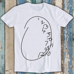 Puede incluir: Camiseta blanca con un contorno negro de una esfera de reloj con los números del 1 al 12 escritos alrededor del borde.