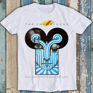 May include: White t-shirt featuring a graphic print of a blue and white face with a globe in one eye. The text "The Chameleons" and "What Does Anything Mean? Basically" is printed on the shirt.