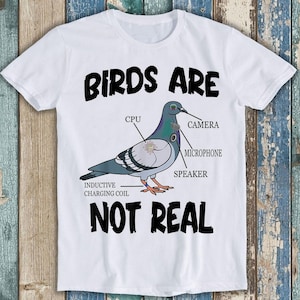 Puede incluir: Camiseta blanca con un gráfico negro de una paloma con varios componentes internos etiquetados. El texto "Birds are not real" está impreso debajo de la paloma.