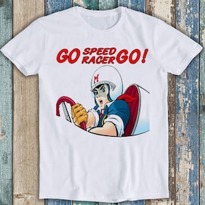 以下が含まれることがあります： 白いTシャツに、赤いレースカーに乗った漫画のキャラクターの赤と白のグラフィックが描かれています。Tシャツには赤い文字で「GO SPEED RACER GO!」と印刷されています。