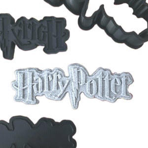Può includere: Un set di quattro tagliabiscotti in plastica nera con il logo di Harry Potter e le parole "Harry Potter".