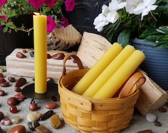 May include: Three yellow beeswax candles in a woven basket with leather handles, surrounded by red and brown stones. A single yellow beeswax candle is on a black metal candle holder.