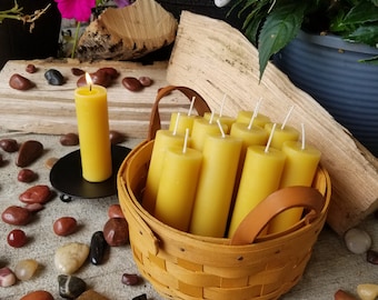 May include: A basket filled with yellow beeswax candles, surrounded by red and brown stones. The candles are arranged in a circular pattern and are ready to be lit.