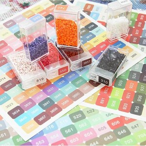 May include: Assortment of small clear plastic containers filled with colourful diamond-shaped beads. The containers are labelled with numbers.