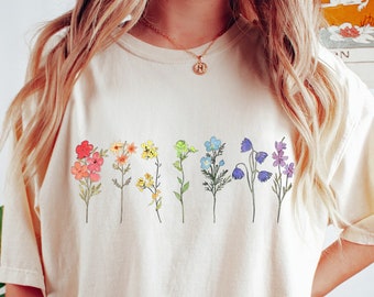 May include: A woman wearing a cream colored t-shirt with a rainbow of flowers printed on the front. She is wearing dark green biker shorts.