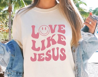 May include: A white sweatshirt with a pink graphic that says "LOVE LIKE JESUS" with a smiley face in the "O" of LOVE.