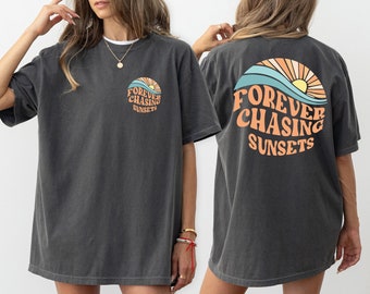 May include: A dark gray oversized t-shirt with a graphic print of a sunset and the text "FOREVER CHASING SUNSETS" on the back. The same graphic is printed on the front of the shirt, but it is smaller.