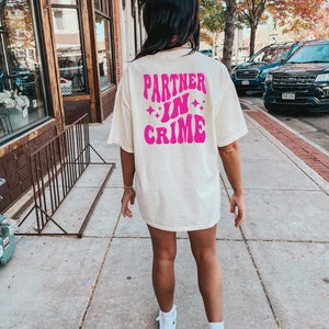 May include: A white t-shirt with a pink graphic that says "Partner in Crime" with stars around the text.