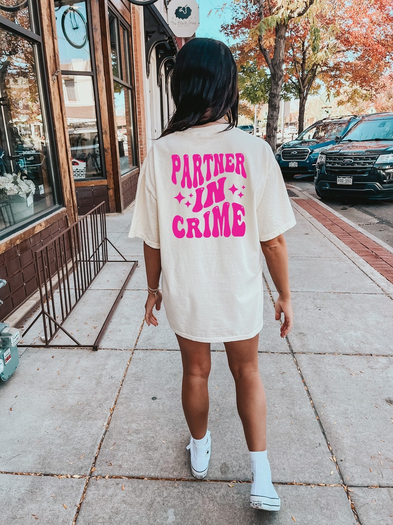 May include: A white t-shirt with a pink graphic that says "Partner in Crime" with stars around the text.