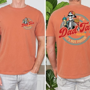 May include: Burnt orange t-shirt with a graphic on the front and back. The front graphic says "Dad Tax" with a skeleton wearing a hat. The back graphic says "Dad Tax Making It's Not Poison" with a skeleton holding fries and a drink.