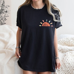May include: A black oversized t-shirt with a colourful sun graphic on the front. The sun is made up of orange, red, yellow, green, and blue colours.