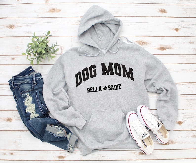 K&ouml;nnte beinhalten: Grauer Kapuzenpullover mit dem Text "Dog Mom" in Schwarz, darunter die Namen "Bella" und "Sadie".