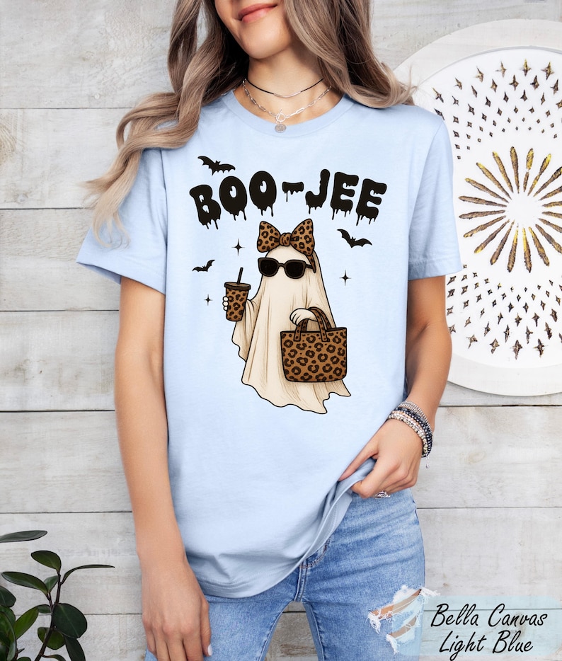 A woman wearing a light blue t-shirt with a graphic design of a ghost holding a drink and sunglasses, along with the text "BOO JEE".