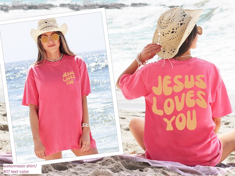 a woman sitting on the beach wearing a pink jesus loves you t - shirt