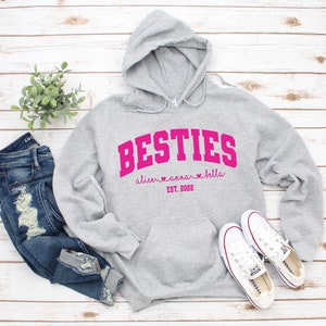 May include: Gray hooded sweatshirt with the text "BESTIES" in pink with the names "alice", "anna", and "bella" and the text "EST. 2022" below.