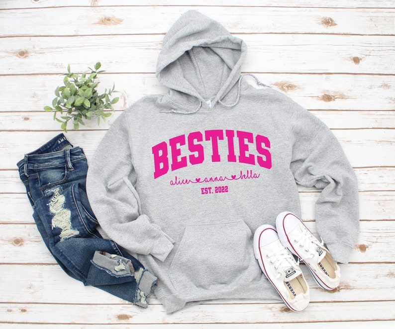 May include: Gray hooded sweatshirt with the text "BESTIES" in pink with the names "alice", "anna", and "bella" and the text "EST. 2022" below.