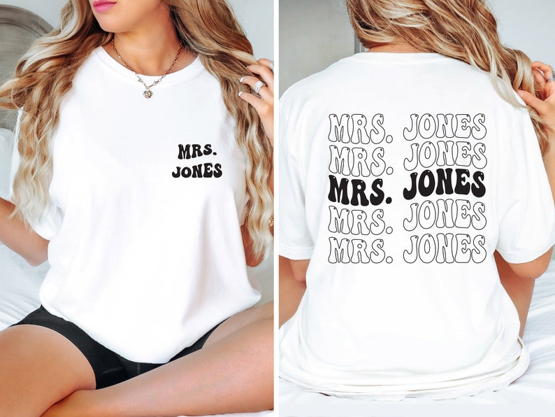 May include: White t-shirt with the text "MRS. JONES" in a retro font on the front and back. The back of the shirt repeats the text multiple times. The text is black and white.