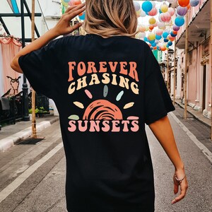 May include: Black oversized t-shirt with a graphic print of a sunset and the text "FOREVER CHASING SUNSETS" in colourful letters.