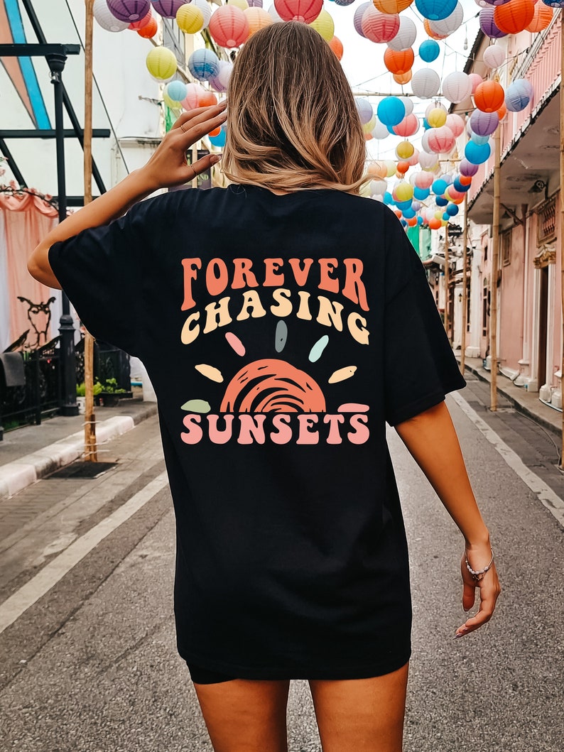May include: Black oversized t-shirt with a graphic print of a sunset and the text "FOREVER CHASING SUNSETS" in colourful letters.