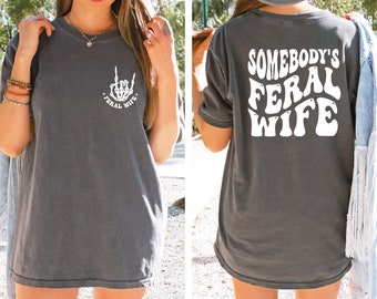 May include: Gray oversized t-shirt with a white graphic of a skeleton hand giving the rock and roll sign with the text "Feral Wife" on the front and the text "Somebody's Feral Wife" on the back.