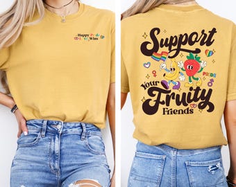 May include: Mustard-colored t-shirt with the text "Happy Pride, Love Wins" on the front. The back of the shirt features the text "Support Your Fruity Friends" with cartoon fruit characters and Pride symbols.