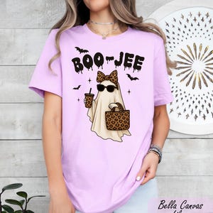 A woman wearing a pink t-shirt with a graphic of a ghost wearing sunglasses and holding a drink.
