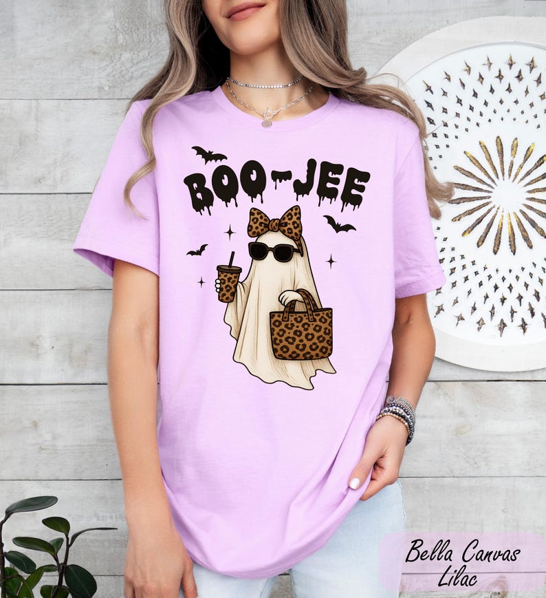 A woman wearing a pink t-shirt with a graphic of a ghost wearing sunglasses and holding a drink.