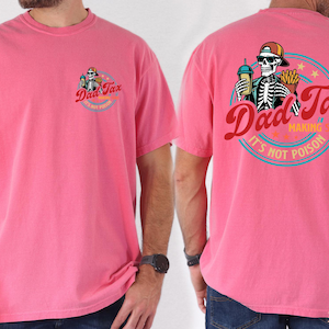 May include: A pink t-shirt with a graphic on the front and back. The front graphic says "Dad Tax" with a skeleton wearing a hat. The back graphic has the same text and a skeleton holding a drink and fries. The text "Making Sure It's Not Poison" is also on the back.