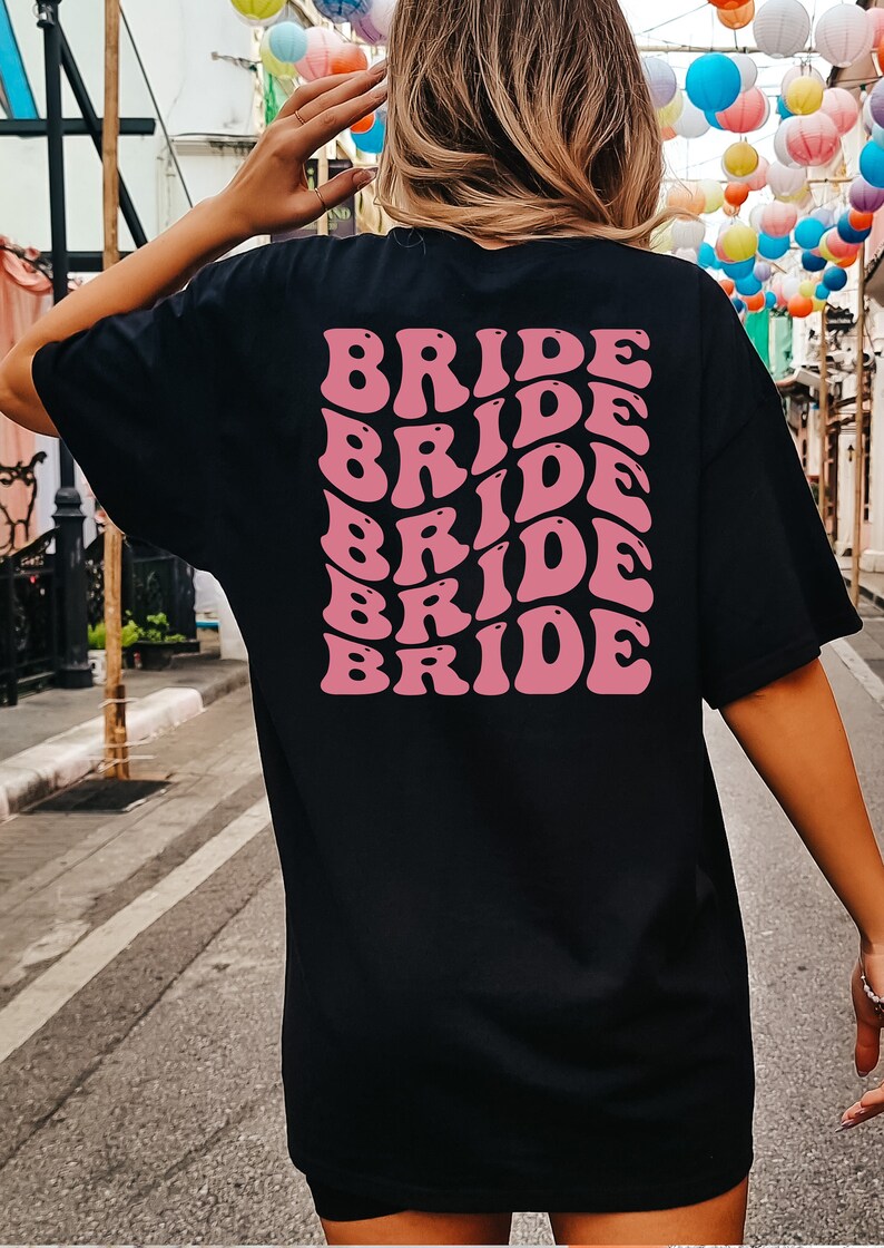 May include: Black t-shirt with the word "BRIDE" repeated in pink, retro-style lettering on the back.