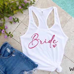 May include: White tank top with the word "Bride" in pink script with a small pink heart.