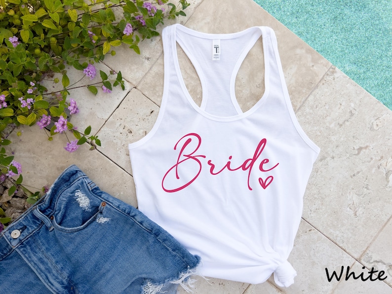 May include: White tank top with the word "Bride" in pink script with a small pink heart.