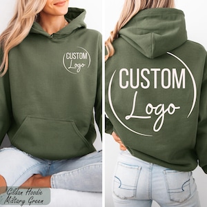 May include: Olive green hoodie with a front pocket and a hood. The front and back of the hoodie feature a white circular design with the words "CUSTOM Logo" in a handwritten style font. The bottom of the image has the text "Gildan Hoodie Military Green".