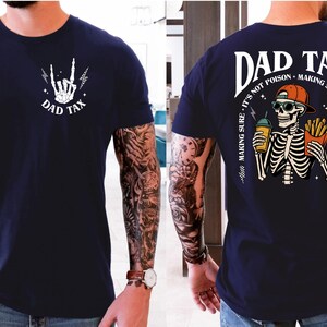 a man wearing a navy blue t-shirt with a graphic design on the back. The design includes a skeleton holding a beer and the text "DAD TAX" along with a humorous message about fatherhood and taxes.