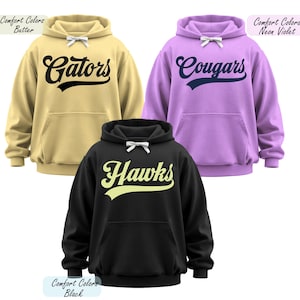 May include: Three hooded sweatshirts in butter, neon violet, and black. Each sweatshirt features a team name in a script font: "Gators", "Cougars", and "Hawks". The sweatshirts have a front pocket and a white bow detail on the hood.
