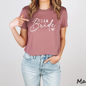 May include: Mauve cropped t-shirt with the text "Team Bride" in white lettering and a small heart.
